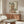 May include: Japanese woodblock print artwork showing a woman in ornate orange and cream kimono holding a decorative fan, displayed in thin wooden frame above mid-century walnut credenza with brass hardware. Modern white curved chair and glass-top oval coffee table visible in bright minimalist room with cream walls and natural lighting.