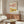 May include: Framed marine illustration print featuring two colorful lobsters - one pink with green spots and one yellow with red spots - displayed above a mid-century modern walnut credenza. Room setting shows white upholstered chair, round glass coffee table, white table lamp, and neutral walls with natural lighting creating shadows.