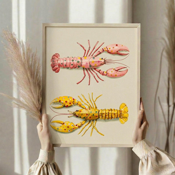 May include: Person holding a framed print featuring two colorful lobster illustrations - one pink with polka dots and one yellow with red spots - against a cream background in a light wood frame. Dried pampas grass visible to the left, soft natural lighting from windows creates gentle shadows on neutral wall.