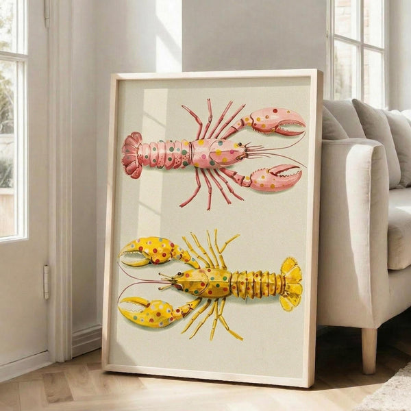 May include: Framed artwork displaying two colorful lobsters with polka dot patterns - one pink with multicolored spots, one yellow with red and blue dots. The illustration shows detailed marine creatures with claws, antennae, and segmented tails on a cream background. Light wood frame leans against white wall near beige upholstered chair in bright, modern living room with large windows casting natural light.