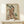 May include: Japanese woodblock print featuring a woman in elaborate orange and cream kimono holding a decorative fan, displayed in light wood frame on pale wooden shelf. Small white wrapped gift with greenery sits beside the framed artwork against cream wall. The vintage-style print shows traditional ukiyo-e art with delicate botanical details and muted earth tones.