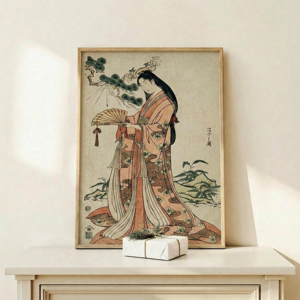 May include: Japanese woodblock print featuring a woman in elaborate orange and cream kimono holding a decorative fan, displayed in light wood frame on pale wooden shelf. Small white wrapped gift with greenery sits beside the framed artwork against cream wall. The vintage-style print shows traditional ukiyo-e art with delicate botanical details and muted earth tones.