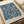 May include: Vintage-style botanical print displayed on wooden surface with cream paper roll. Features intricate blue floral pattern with sunflowers, grapes, and ornate leaves on cream background. Text reads "MORRIS & COMPANY 1866" and "WILLIAM MORRIS" at bottom. Victorian-inspired decorative wallpaper design in navy blue against neutral tones.