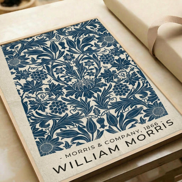 May include: Vintage-style botanical print displayed on wooden surface with cream paper roll. Features intricate blue floral pattern with sunflowers, grapes, and ornate leaves on cream background. Text reads "MORRIS & COMPANY 1866" and "WILLIAM MORRIS" at bottom. Victorian-inspired decorative wallpaper design in navy blue against neutral tones.