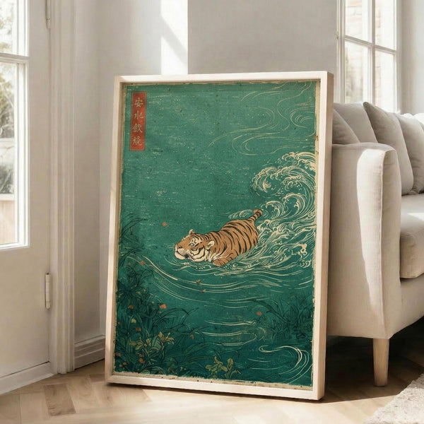 May include: Framed Japanese-style artwork featuring an orange and black striped tiger swimming through turquoise-green water with white foam waves, displayed in a light wood frame leaning against a white wall next to a beige upholstered chair in a bright living room with large windows and wooden floors.