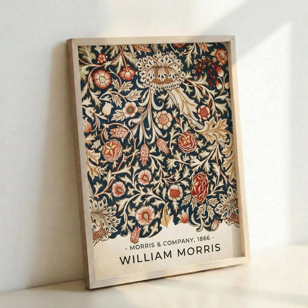 May include: Framed poster print featuring ornate Victorian floral pattern with navy blue background and cream, coral, and rust colored flowers and leaves in William Morris style, displayed in light wood frame leaning against white wall corner