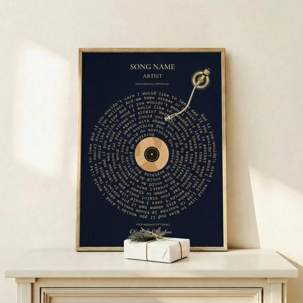 May include: A framed navy blue poster with gold text displaying song lyrics arranged in a spiral pattern around a central vinyl record image, positioned on a light wood shelf next to a small white wrapped gift with twine and greenery, against a cream colored wall.