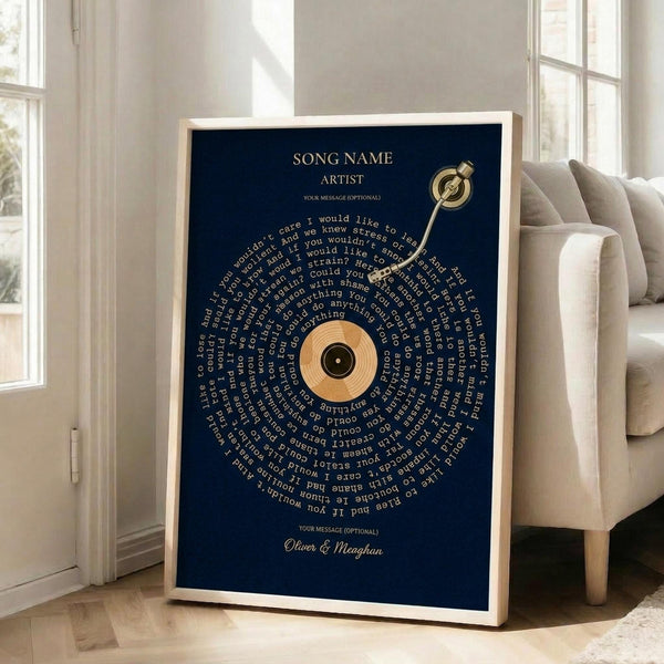 May include: Framed navy blue poster with golden vinyl record design featuring song lyrics arranged in curved text around a central orange and black record. Brass-colored tonearm extends from top right. White text at top shows placeholder song and artist name, with names Oliver & Meaghan at bottom. Light wood frame leans against white wall beside beige upholstered chair in bright, minimalist living room with white walls and large windows.