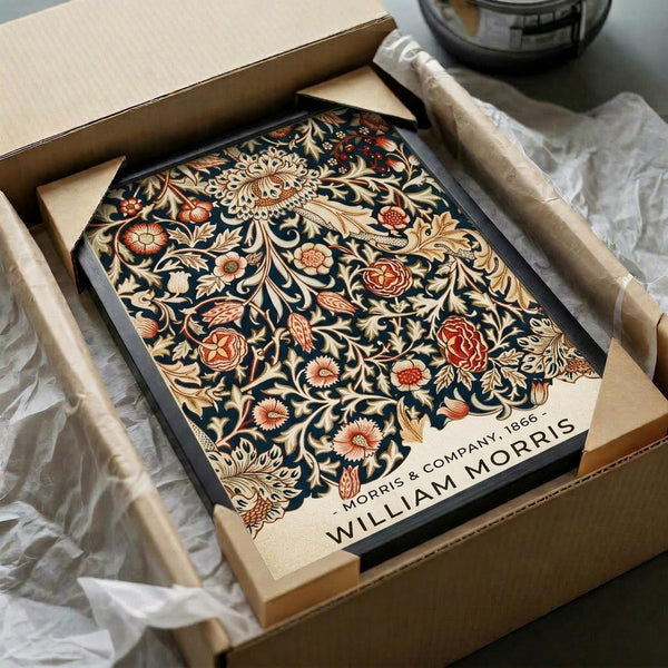 May include: Ornate Victorian-style botanical poster with intricate floral patterns in navy blue, cream, and rust colors featuring roses, chrysanthemums, and decorative foliage. Black-framed artwork displayed in open cardboard shipping box with protective tissue paper wrapping, sitting on white fabric surface next to dark glass vessel.