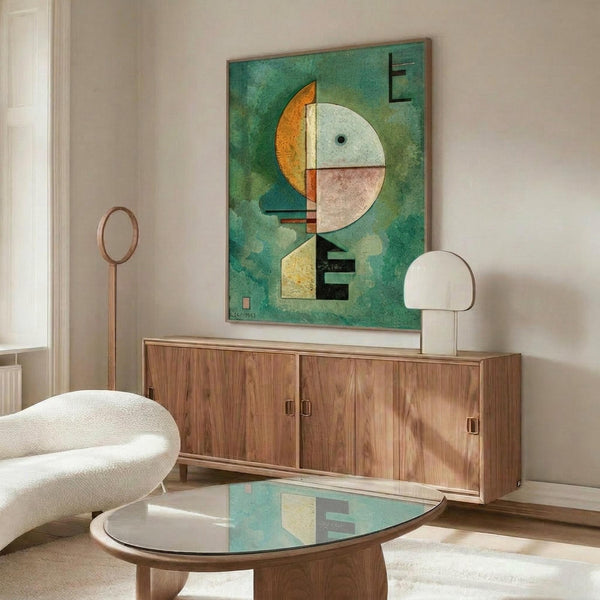 May include: Abstract modernist artwork with geometric shapes in green, orange, and pale colors displayed above a wooden sideboard in a minimalist living room. The framed print features circular and angular forms against a textured green background. White upholstered chair and glass coffee table complete the mid-century modern setting with natural lighting.