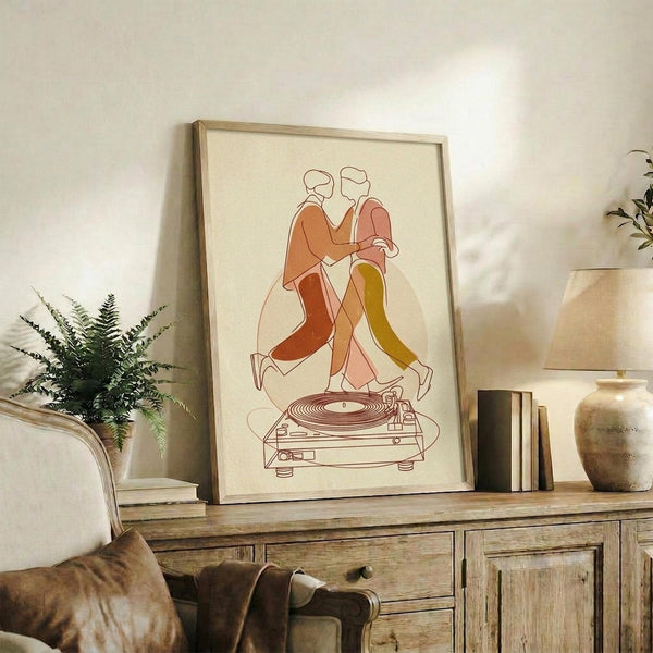 May include: Framed minimalist line art poster showing two dancing figures in orange, pink, and yellow tones above a turntable, displayed on rustic wood credenza alongside fern plant, books, and ceramic vase in warm-toned living room setting