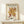 May include: Matisse cut-outs exhibition poster in light wood frame leaning against white wall on natural wood shelf. Features abstract coral and golden yellow organic shapes resembling sea anemones or coral formations on cream background. Text reads "MATISSE THE CUT-OUTS" and "BERGGRUEN & CIE" with Paris gallery details. Small wrapped gift with evergreen sprig sits beside frame.