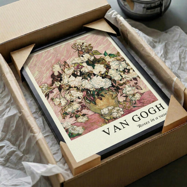 May include: Framed Van Gogh roses print in black frame being unpacked from cardboard shipping box with protective tissue paper. The artwork shows white and pink roses in a yellow vase against a textured pink background. Wooden frame pieces and packing materials scattered around on white surface, creating an unboxing scene that demonstrates how the vintage-style floral art print arrives to customers.