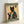 A framed poster featuring a black cat with yellow eyes wearing a traditional Japanese kimono in teal with orange floral patterns. The cat holds a steaming red coffee cup while sitting formally. The artwork is styled like vintage Japanese woodblock prints with aged beige background and Japanese characters. Green banners at top and bottom read "MORE ESPRESSO" and "LESS DEPRESSO" in cream lettering. The wooden frame sits against a white wall.