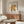May include: Matisse cut-outs exhibition poster in thin wooden frame hanging above walnut credenza in modern living room. Poster features yellow and burgundy organic coral-like shapes on cream background with black text reading "Matisse The Cut-Outs" and "Berggruen & Cie" with 1953 exhibition details. Room styled with white curved chair, brass floor lamp, glass coffee table, and warm lighting creating poster reflection on glossy surface.