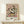 May include: Framed poster print of Van Gogh's white roses painting displayed on light wood surface against cream wall. The artwork shows abundant white roses with pink and green accents in an impressionist style with visible brushstrokes. Small wrapped white gift box with green sprig sits beside the natural wood frame.