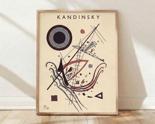May include: Framed abstract art print in light wood frame leaning against white wall on wooden floor. Artwork features geometric shapes in black, red, and gray on cream background - prominent concentric circles in upper left, intersecting lines, curved forms, and small scattered elements throughout. Kandinsky's signature visible in bottom left corner.