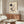 May include: Kandinsky abstract art print displayed above a wooden credenza in a modern living room. The poster features geometric shapes, circles, lines and curves in black, red, and muted tones on cream background. Room shows white textured chair, glass-top coffee table, and minimalist decor with natural lighting creating shadows on polished floors.