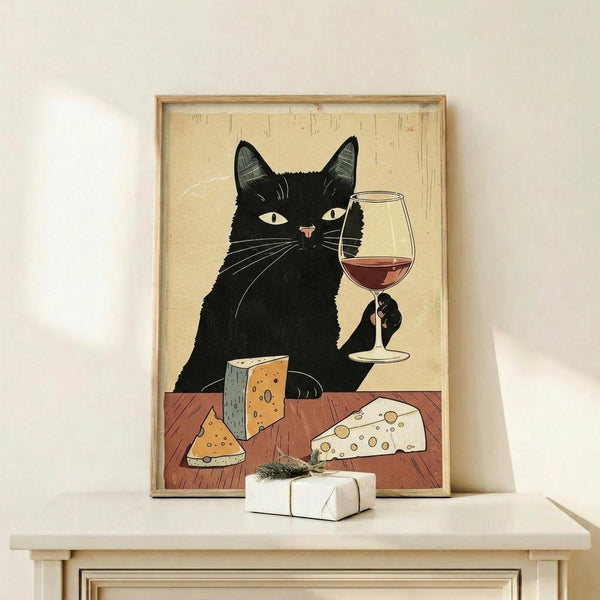 May include: Framed poster print displayed on light wood shelf showing black cat holding wine glass with red wine, surrounded by various cheese wedges on wooden table. Artwork features vintage-style illustration with beige background and warm earth tones. Small white wrapped gift with greenery sits on shelf beside the natural wood frame.