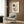 May include: Framed Kandinsky abstract art print hanging on wood-paneled wall above cream upholstered armchair with geometric pillow. Print features black circles, red triangles, and intersecting lines on cream background. Modern brass floor lamp and dark side table with open book complete the warm, contemporary room setting.
