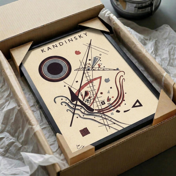 May include: Framed abstract art print in beige, black and burgundy tones featuring geometric shapes, lines, circles and curved forms in Kandinsky's distinctive style. The black-framed artwork sits in an open cardboard shipping box with white tissue paper, alongside wooden dowels used for packaging protection.
