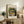 May include: Framed Matisse museum poster featuring a colorful still life of goldfish in a glass bowl surrounded by leafy plants, displayed on a rustic wooden sideboard next to a fern plant, ceramic vases, and books in a cozy living room setting with neutral tones and natural lighting