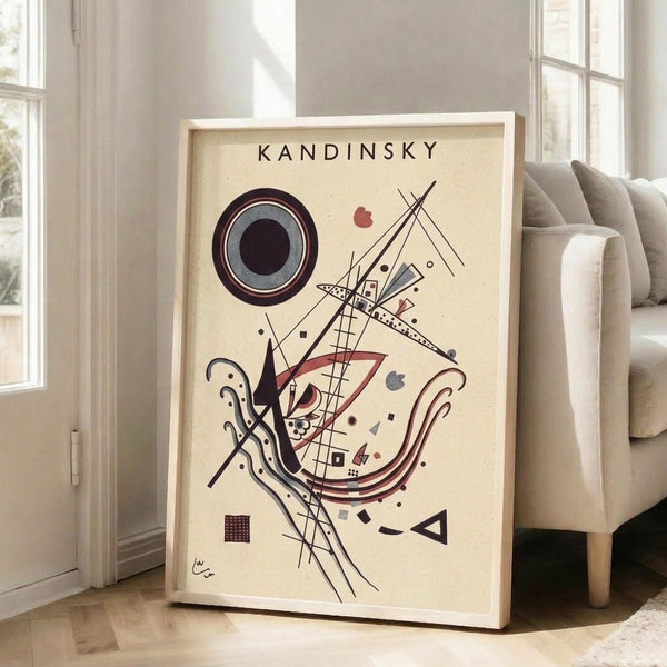May include: Framed abstract art print with cream background featuring geometric shapes in burgundy, black, and gray. Shows concentric circles, angular lines, curved forms, and small squares in Kandinsky's distinctive style. White frame leans against wall next to beige upholstered chair in bright, modern living room with large windows.