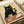 A vintage-style illustration of a black cat with yellow eyes holding a wine glass filled with red wine. The cat sits at a wooden table with various cheese wedges and slices scattered around. The artwork has a cream-colored background with woodblock print aesthetic. The print is displayed flat on white paper with a beige ribbon visible in the corner, showing the actual poster artwork itself.
