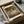 May include: Framed art print of Claude Monet's impressionist garden painting featuring vibrant purple, pink and green flowering plants beneath drooping willow trees. The cream-colored print with black frame sits in an open cardboard shipping box with white tissue paper, next to wrapped cylindrical items on a neutral surface.