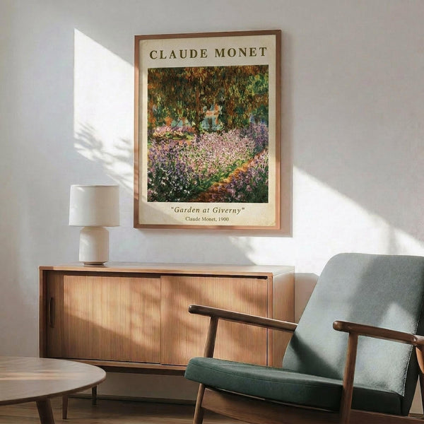 May include: Framed Claude Monet poster print showing garden scene with purple irises and lush greenery, displayed above wood sideboard with white ceramic lamp in modern living room setting with sage green upholstered armchair and natural sunlight casting shadows on white wall