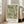 May include: Framed botanical art print with William Morris floral pattern in sage green, coral orange, and cream tones, displayed on light wood floor next to beige sofa in bright room with white walls and windows. The vintage-style design features intricate leaves and clustered flowers throughout.
