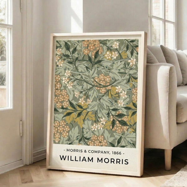 May include: Framed botanical art print with William Morris floral pattern in sage green, coral orange, and cream tones, displayed on light wood floor next to beige sofa in bright room with white walls and windows. The vintage-style design features intricate leaves and clustered flowers throughout.