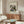 May include: Framed Kandinsky abstract art print hanging above wooden sideboard in modern living room. Artwork features dynamic composition of intersecting black lines, geometric shapes, and vibrant colors including red, blue, yellow on cream background. White upholstered chair and glass coffee table visible in foreground, creating mid-century modern interior styling.