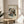 May include: Framed abstract art print with geometric shapes, lines, and colorful elements in Kandinsky's distinctive style displayed on a light wood round side table. Cream colored walls with natural sunlight streaming through window, beige upholstered chair partially visible, and green plant leaves in corner create a minimalist modern living space setting.