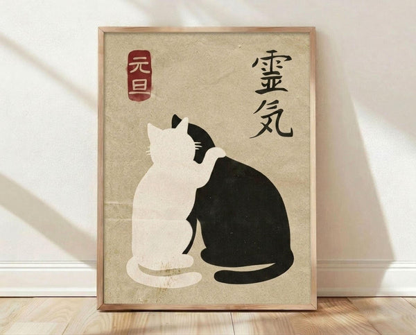May include: Framed poster print leaning against white wall on wooden floor. Artwork features two cats in yin-yang formation on textured beige background - one white cat and one black cat sitting back-to-back with curved tails creating circular balance. Japanese characters appear on right side with red rectangular seal stamp on left. Light wooden frame surrounds the minimalist Asian-inspired design.