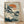 May include: Framed Japanese woodblock print artwork leaning against white wall on light wooden floor. The vintage-style illustration shows white cranes or herons among pine trees beside water, with orange sun in background and vertical Japanese text banner. Artwork has muted teal, orange, and cream colors in traditional ukiyo-e style, displayed in natural wood frame.