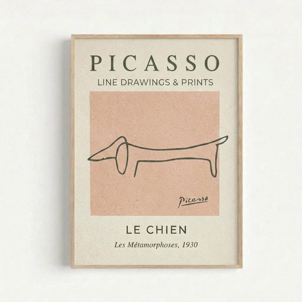 A framed minimalist line drawing of a dachshund dog created with a single continuous black line on a peachy-pink square background. The artwork is displayed in a light wood frame against a cream-colored mat. Text above reads "PICASSO LINE DRAWINGS & PRINTS" and below shows "LE CHIEN" with "Les Métamorphoses, 1930" along with Picasso's signature. The frame hangs on a white wall.