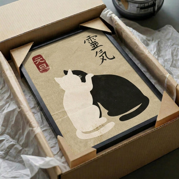 May include: Framed artwork featuring two cats in yin yang formation - one white, one black - on beige textured background with Japanese characters and red stamp seal. Black frame sits in open cardboard shipping box with tissue paper padding and wooden rolling tubes nearby on white surface.