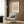 May include: Framed poster with beige background featuring minimalist black line drawing of a dachshund dog, titled "PICASSO LINE DRAWINGS & PRINTS" and "LE CHIEN Les Métamorphoses, 1930". Displayed in modern living room with light gray upholstered chair, geometric patterned pillow, gold floor lamp, dark round side table with open book, and wood panel wall.