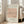 May include: Framed beige and peach poster featuring minimalist black line drawing of a dachshund dog in continuous line art style, displayed leaning against white wall next to light gray upholstered sofa in bright, airy room with large windows and natural lighting on wooden floors.