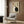 May include: Framed poster featuring two cats in yin yang pose - one white, one black - with Japanese characters on beige textured background, displayed above beige armchair with geometric pillow in modern living room with wood paneled walls, brass floor lamp, and side table with open book.