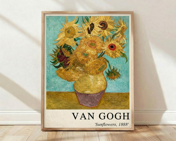 May include: Framed poster print of Van Gogh's famous sunflowers painting displayed on wooden floor against white wall. The artwork shows vibrant yellow sunflowers in a yellow ceramic vase against turquoise background, with thick expressive brushstrokes characteristic of post-impressionist style. Natural wood frame surrounds the print, which includes "VAN GOGH" and "Sunflowers, 1888" text below the image.
