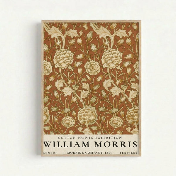 Framed botanical poster featuring William Morris textile design with ornate floral pattern in rust brown and cream colors. Shows detailed flowers, leaves, and vines in Victorian Arts and Crafts style. Text at bottom reads "Cotton Prints Exhibition William Morris London Morris & Company 1861 Textiles" in black lettering on cream background. Natural wood frame against white wall.