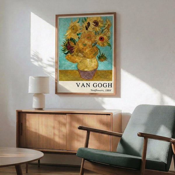 May include: Van Gogh's Sunflowers reproduction poster in thin brown frame hanging on white wall above wooden sideboard. Vibrant yellow sunflowers in vase against turquoise background with artist name and date below. Mid-century modern room with teal upholstered chair, round wood coffee table, white ceramic lamp. Natural sunlight creates diagonal shadows across wall and furniture.