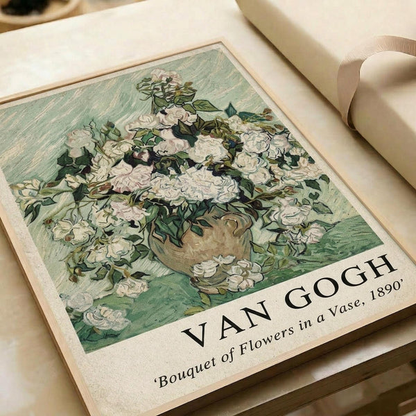 A vintage-style art print featuring white roses in a brown vase against a soft green background, displayed on cream-colored paper with "VAN GOGH" and "Bouquet of Flowers in a Vase, 1890" printed below the image. The print sits on a light wooden surface next to rolled white paper, showing the painterly brushstroke style characteristic of Van Gogh's floral still life works.