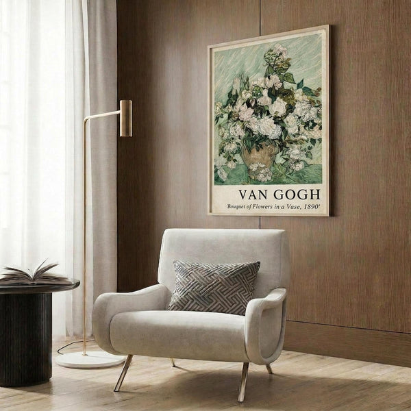 May include: Van Gogh floral poster print in light wood frame mounted on warm brown wood paneled wall above cream upholstered armchair with geometric patterned pillow. Golden brass floor lamp with white circular base stands nearby next to dark round side table with open book. Soft natural lighting from window with sheer curtains creates cozy modern reading nook atmosphere.