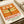 May include: Vintage-style poster print with orange background featuring detailed green dragonfly illustration and Japanese text. Shows "DRAGONFLY" and "KYOTO SCIENCE MUSEUM 2005年4月16日" in red and green lettering. Print displayed in white matted frame on light wooden surface next to rolled paper tubes, creating warm natural lighting and artistic flat lay composition.