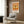 May include: Orange and cream vintage-style poster featuring detailed dragonfly illustration with Japanese text, displayed in white frame on wood-paneled wall above beige upholstered chair with geometric patterned pillow, beside brass floor lamp and dark round side table with open book.