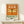 May include: Framed poster with orange and green design featuring detailed dragonfly illustration with translucent wings displayed on light wooden shelf against white wall. Japanese text at top, "DRAGONFLY" and "KYOTO SCIENCE MUSEUM" with date 2005年4月16日 below. Small wrapped gift box with evergreen sprig sits in front of natural wood frame.