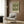 May include: Framed botanical print with intricate green acanthus leaf pattern on cream background, displayed on wood paneled wall above beige upholstered armchair with geometric throw pillow. Modern brass floor lamp and side table with open book complete the neutral-toned reading nook with curtained window.